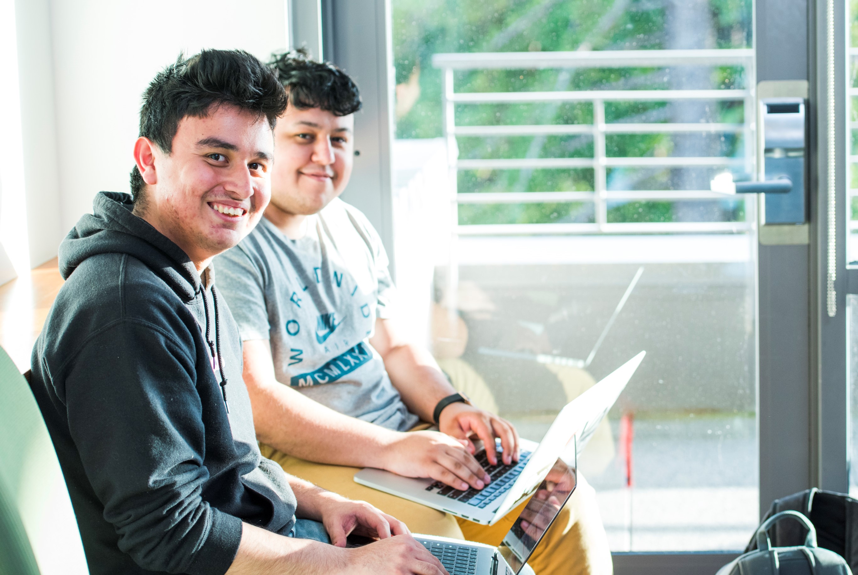 Two smiling college students balancing laptops on their laps.