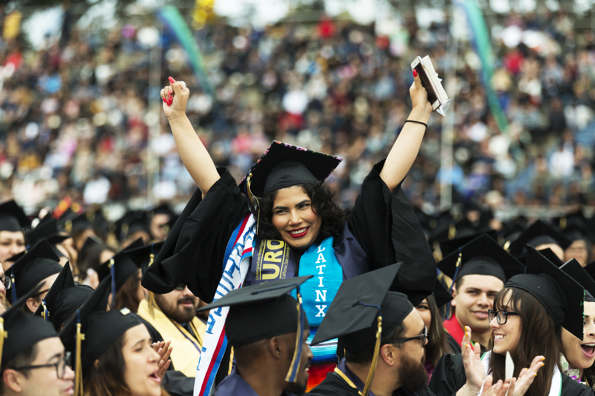 Female graduate raises both arms in triumph at Cal State Monterey Bay