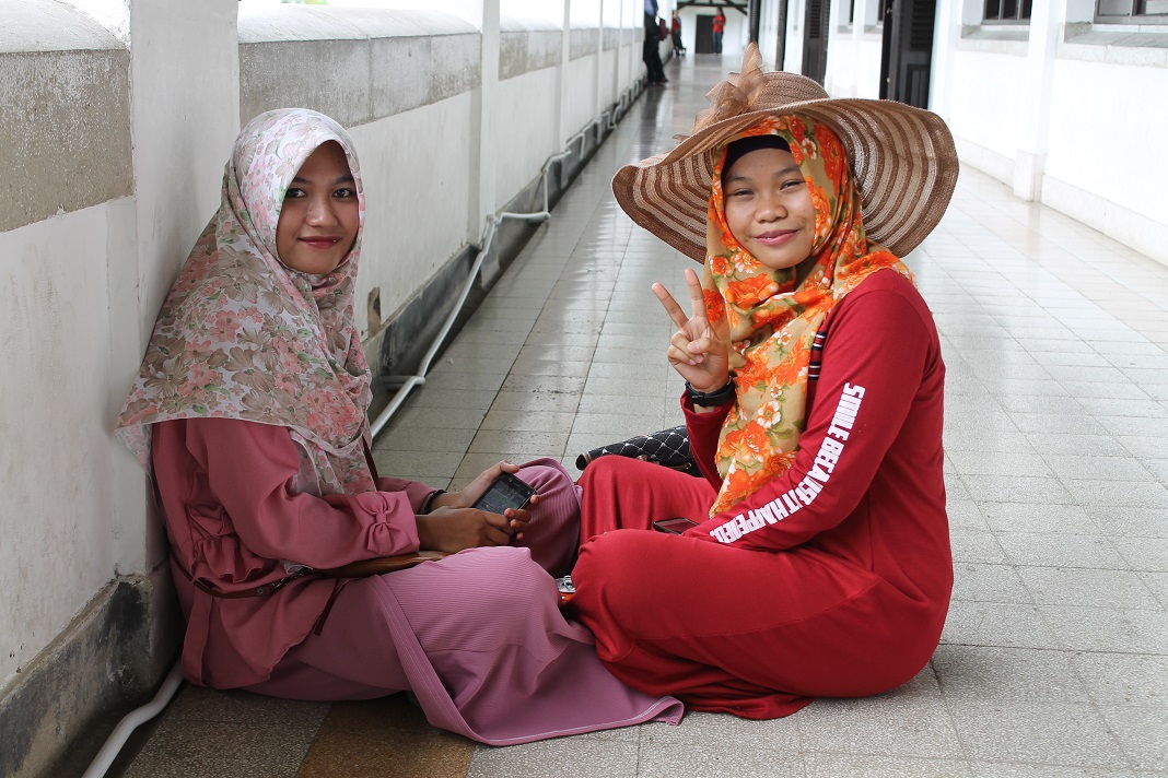 Two women wearing head scarves one giving a peace sign