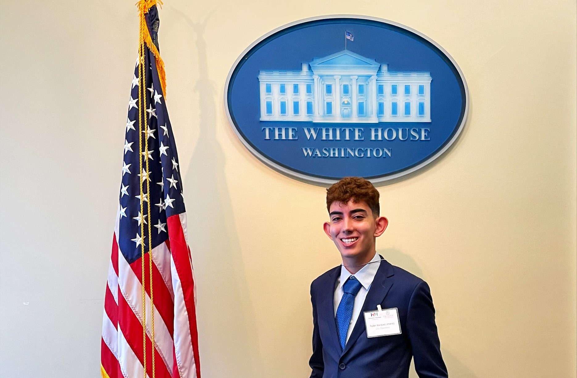 a young person wearing a suit posing in front of a photo of the white house