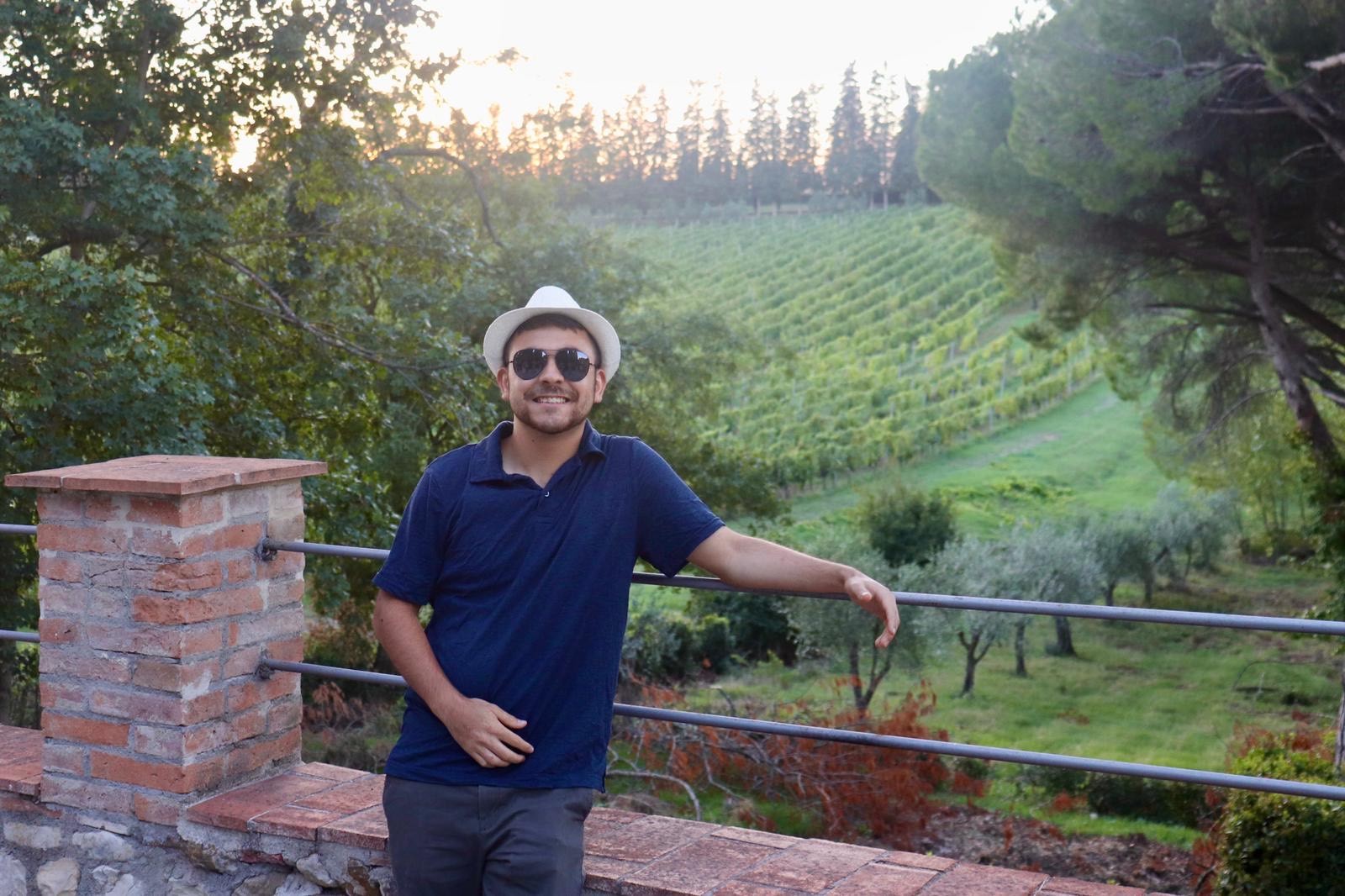 A young person posing in front of rows of grapes growing at a vineyard