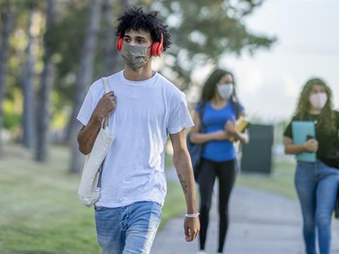 young man walking outside with face mask and headphones
