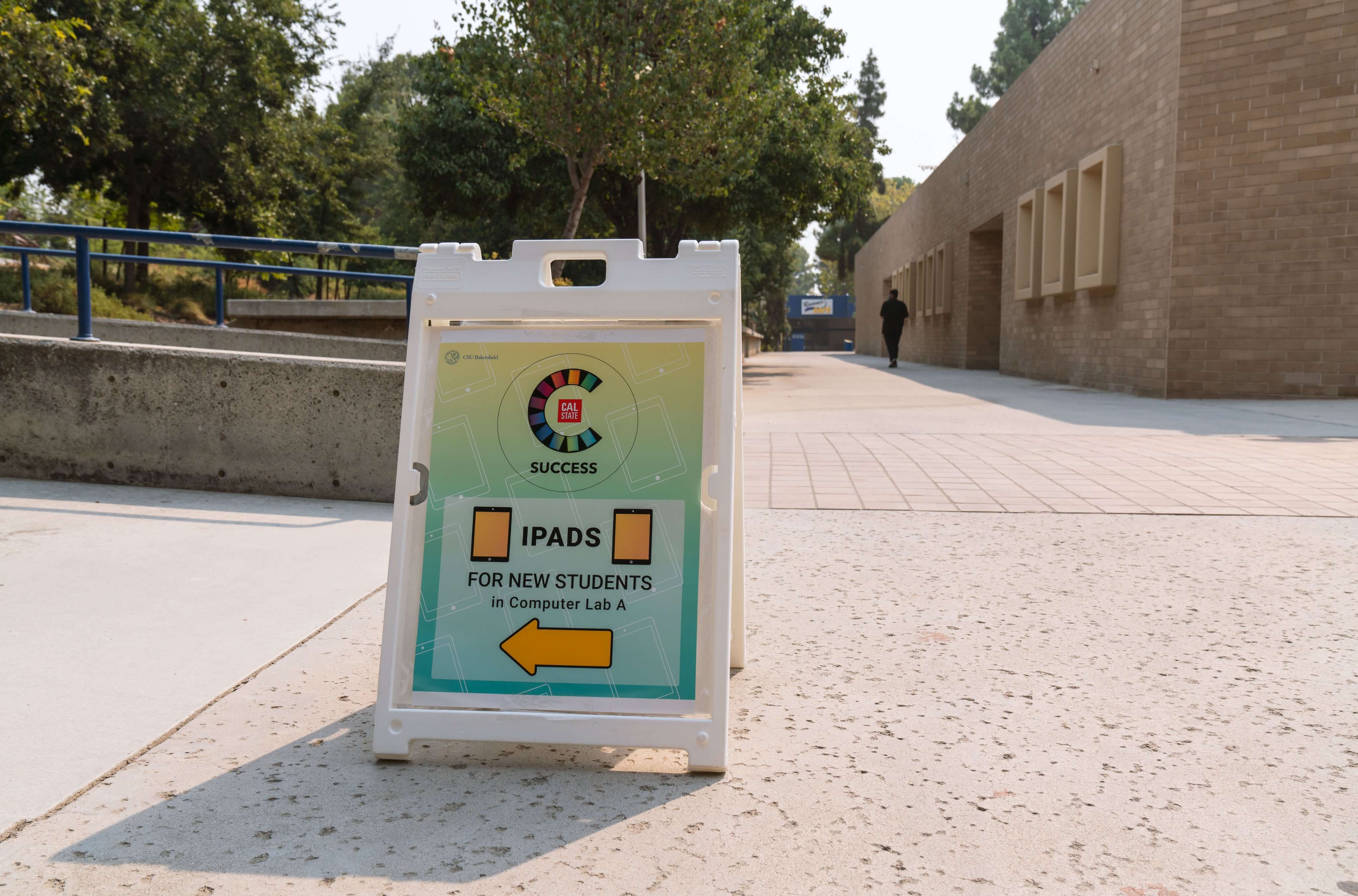easel sign advertising new ipads for students sits on concrete pathway of a college campus