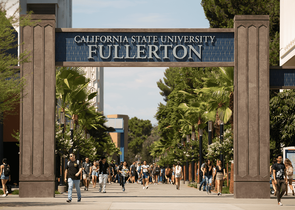 Students walking on campus under archway that reads "California State University Fullerton".