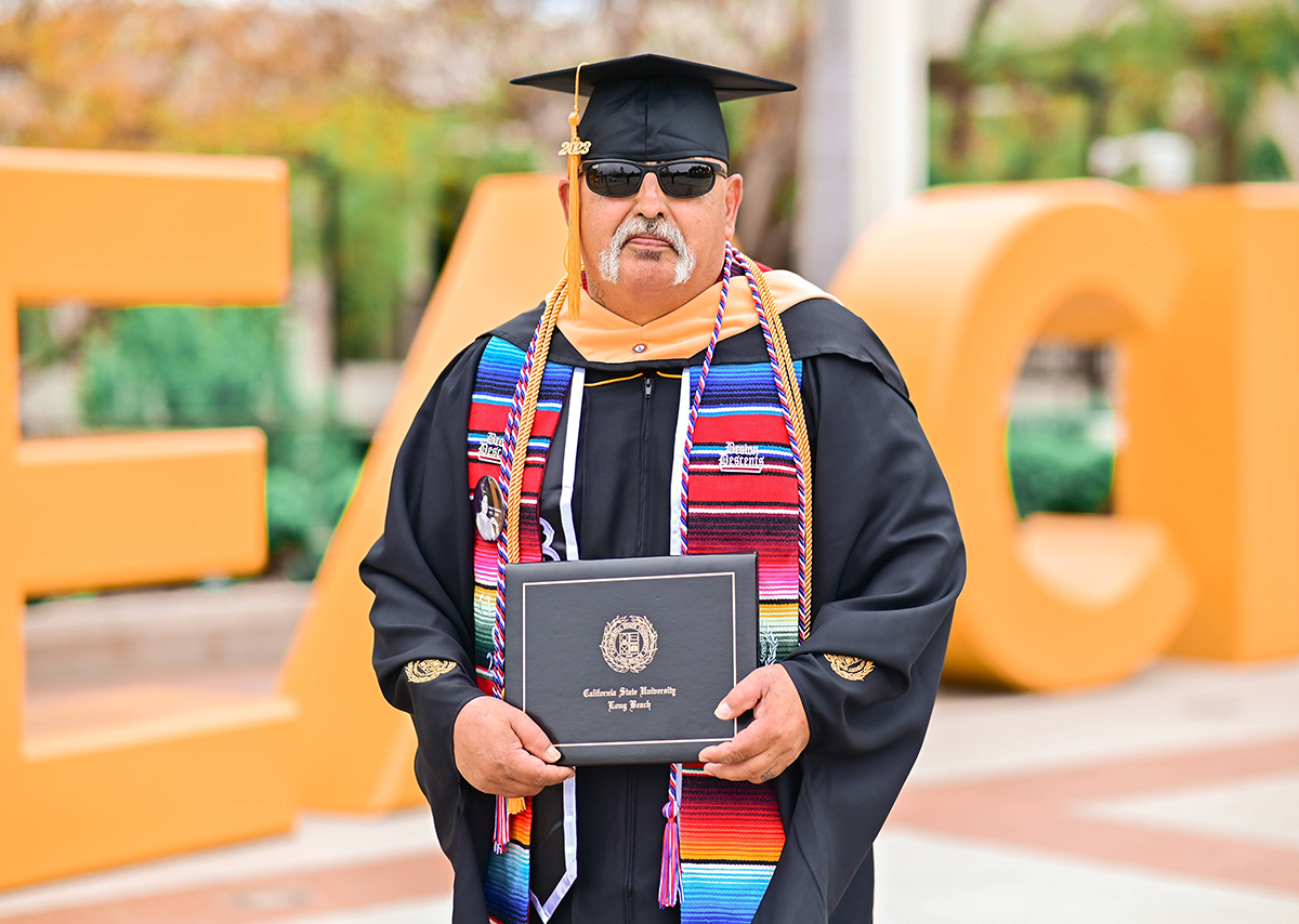 Joseph Valadez posing with sunglasses on in his CSULB graduation cap and gown.