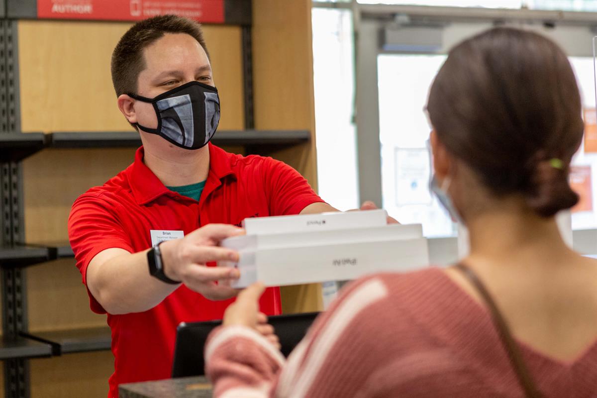 man in protective face masks hands a stack of white boxes to a person in front of counter