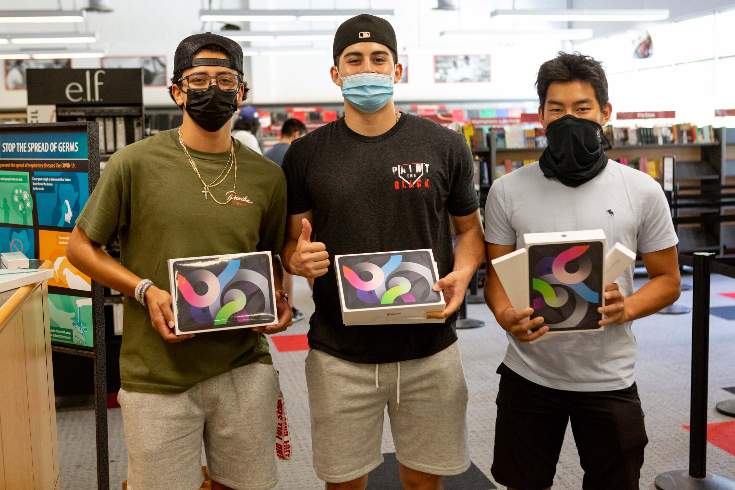 Three male students stand in a row holding up their new boxed iPads. 