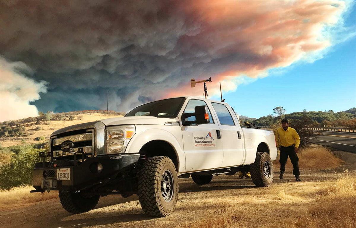 pickup truck with man standing outside near with wildfire smoke in background
