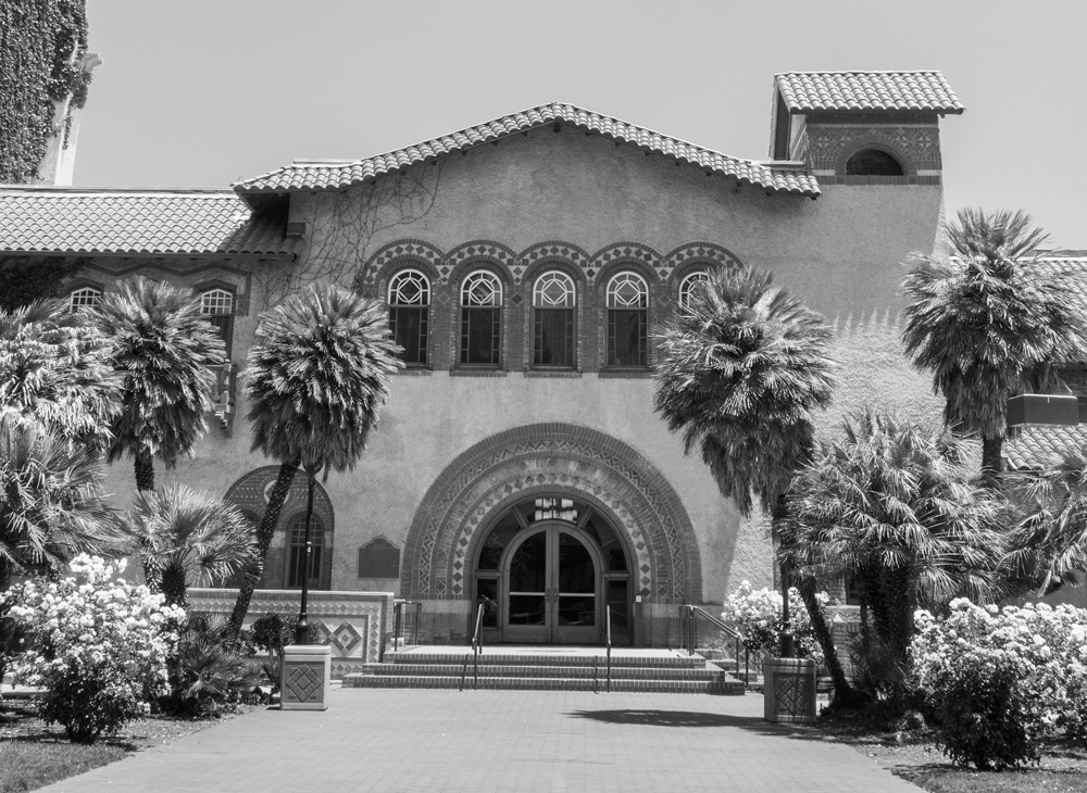 A spanish style building surrounded by palm trees and flower bushes