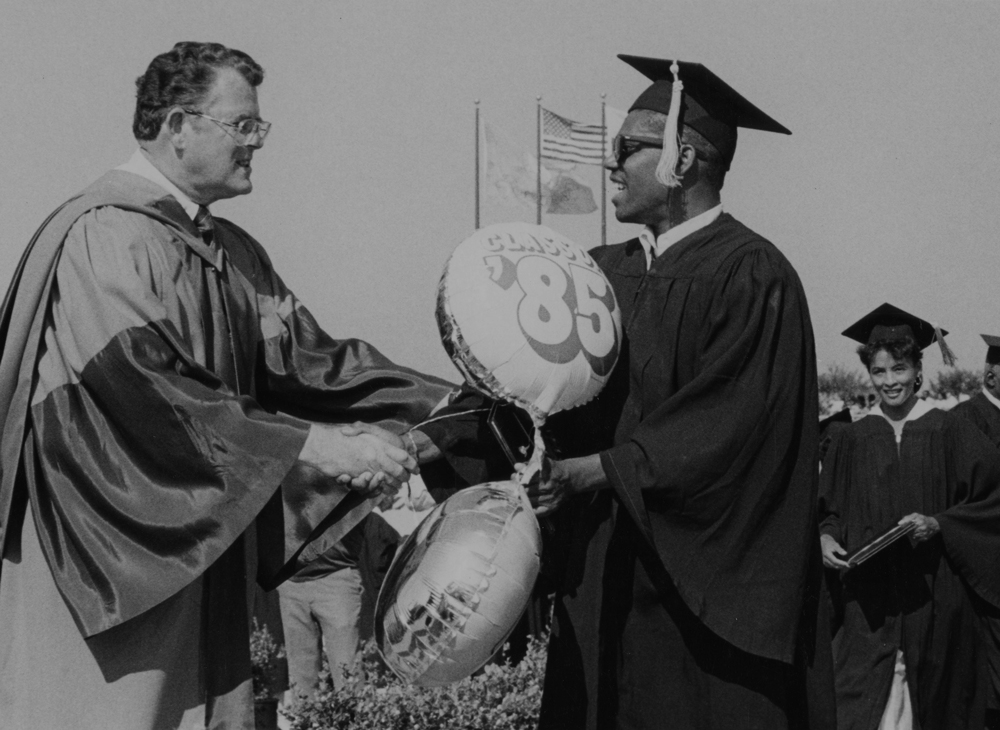 A male student graduating shaking hands with an educator
