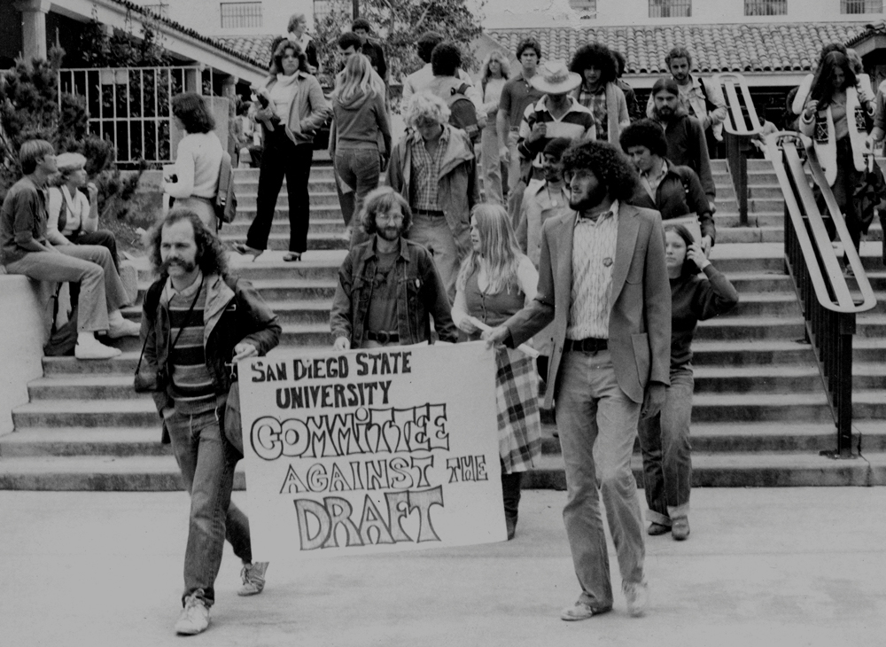 A group of students holding a protesting sign walking through San Diego State University