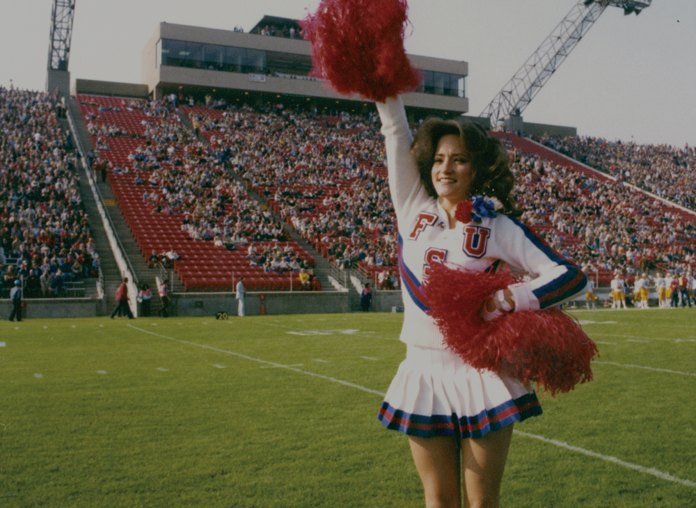 A female cheerleader raising a pom pom during a college football game