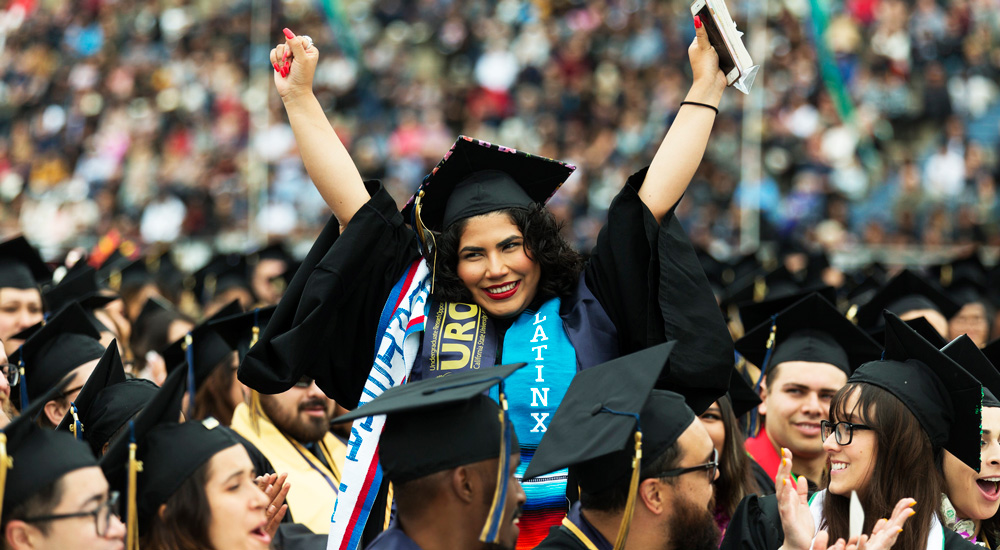 A student throws her arms in the air in celebration at graduation.