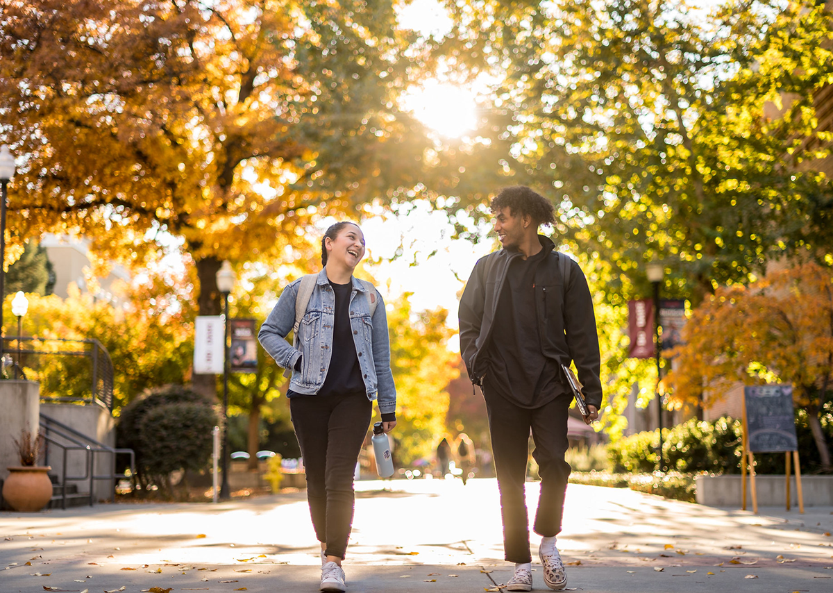 Two students walking on campus surrounded by trees in the middle of fall
