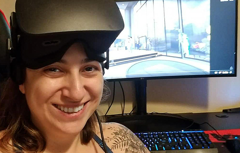 A woman sits at a computer with a VR headset on.