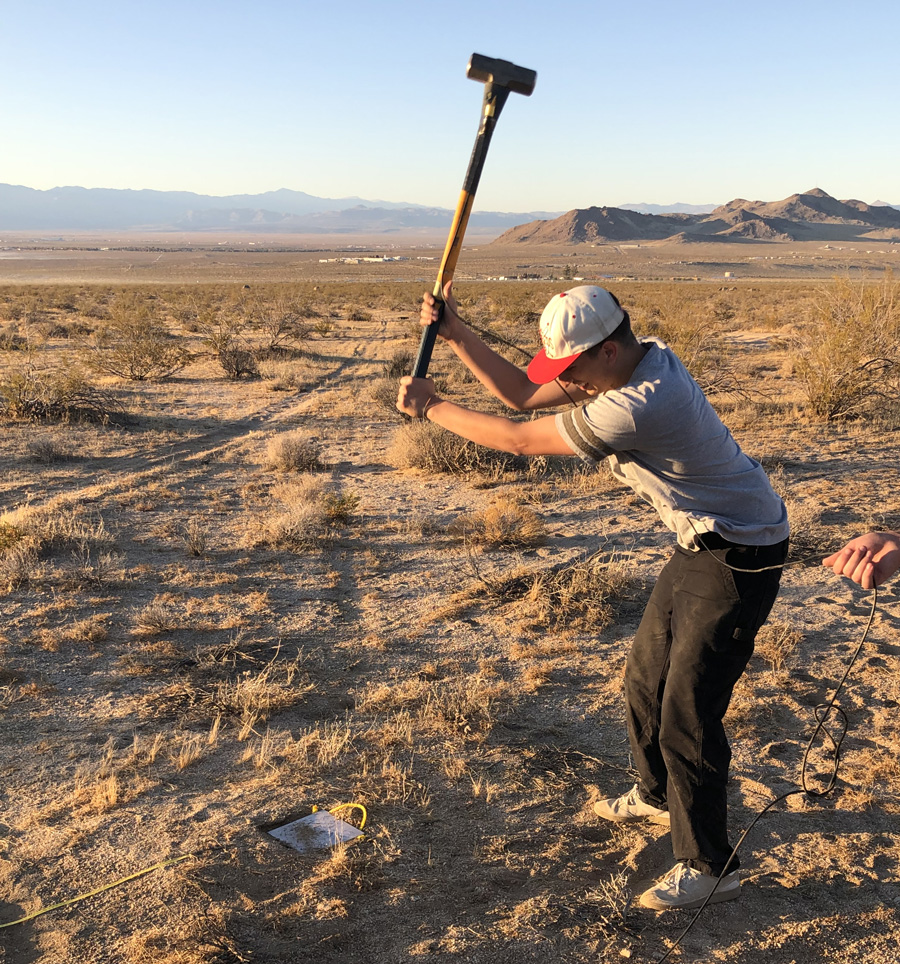 CPP student James East swinging a hammer, which acts as a seismic source, for a refraction experiment to determine the width of the Ridgecrest fault zone during a field class