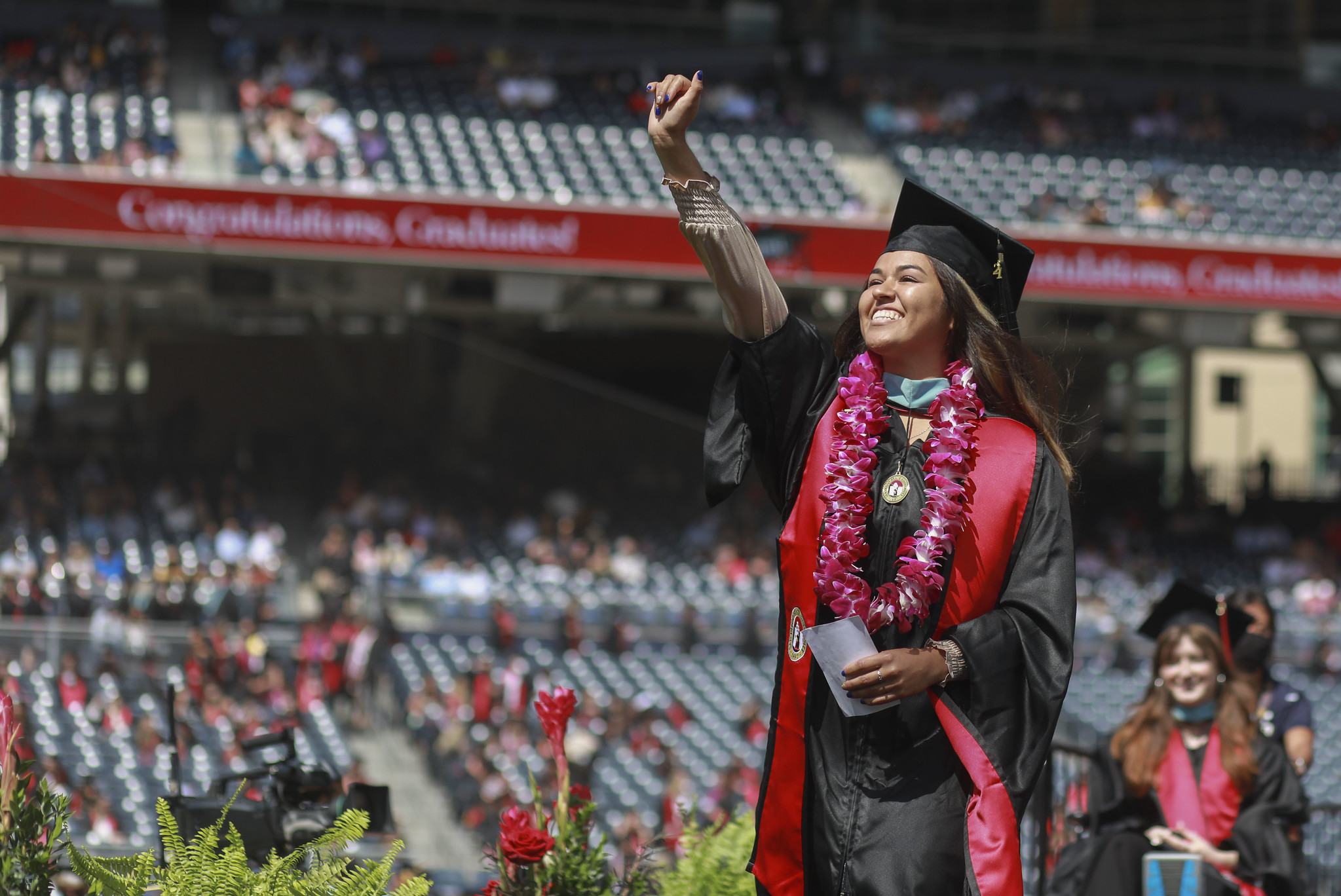 Woman wearing graduation robe and cap with hand in the air in triumph and celebration at a university commencement ceremony.