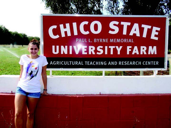 Blakeley Green in a field smiling in front of a red Chico State University Farm sign