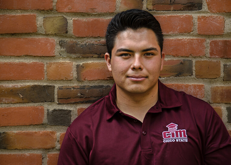 German Fuentes smiling in front of a brick wall wearing a burgundy polo shirt