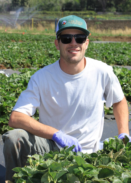 Jonathan Winslow wearing a white shirt smiling in a field of agriculture