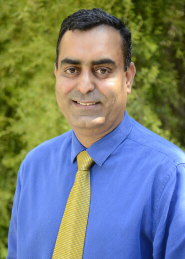 Dr. Gurreet Brar smiling wearing a blue shirt and yellow tie