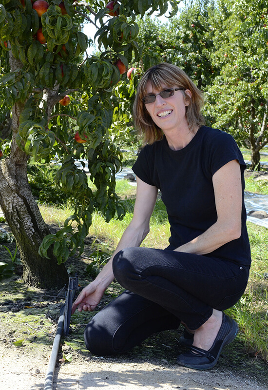 Dr. Florence Cassel Sharma wearing all black smiling in front of a fruit tree