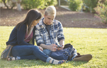 couple looking at phone while sitting on campus grass