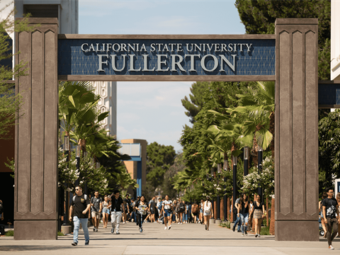 Students walking on campus under archway that reads &quot;California State University Fullerton&quot;.