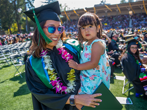 Cal Poly Humboldt student at graduation holding her daughter.