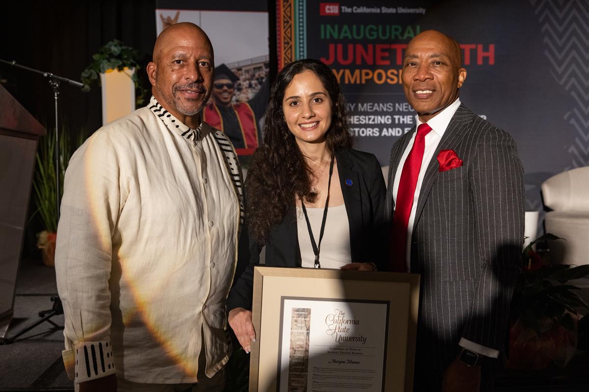 two men and a young woman pose with a framed document