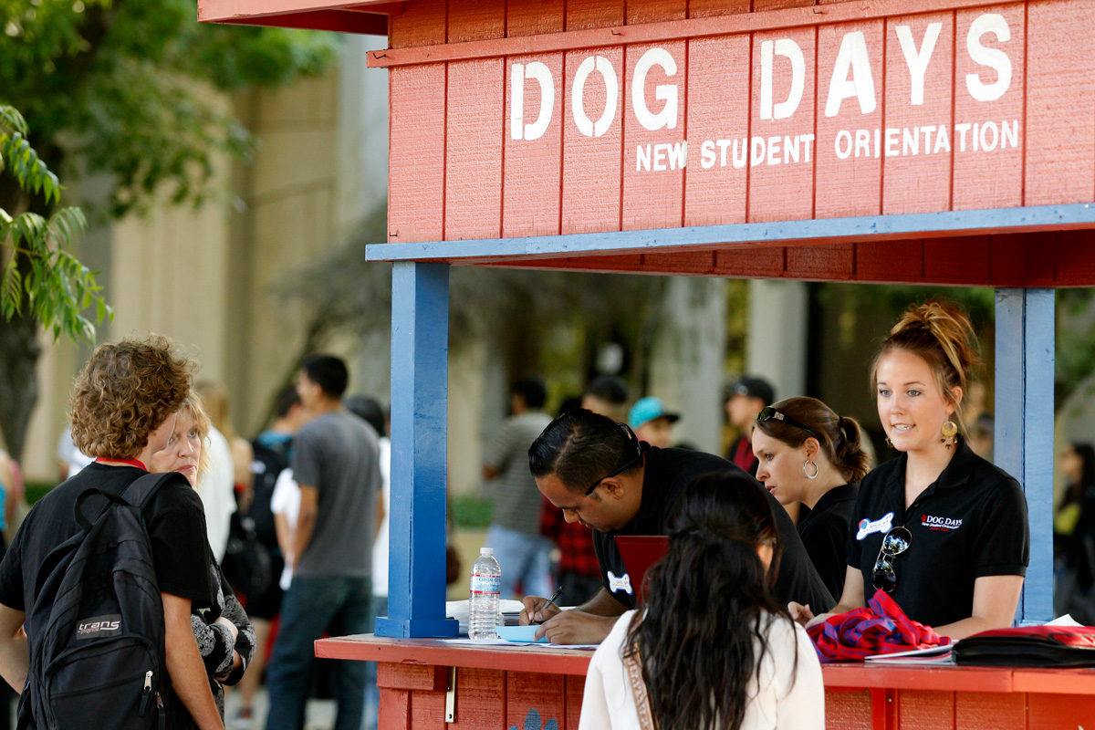 A campus ambassador at a booth helps a student during Fresno State’s Dog Days: New Student Orientation.