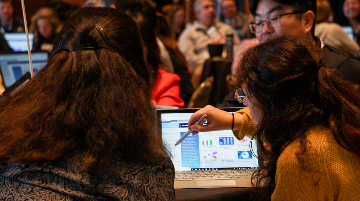 Program participants facing a laptop computer, one student has a stylis pen in her hand pointing to the screen