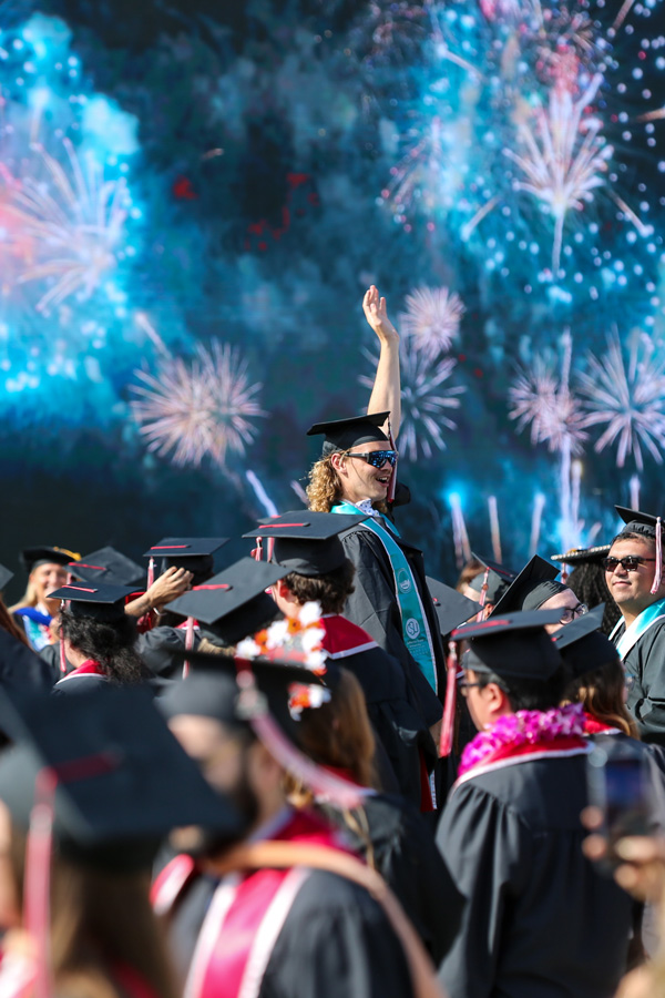 graduating student raising hand in celebration in front of fireworks