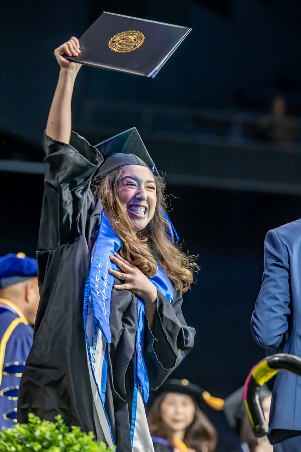 graduating student holding diploma up in celebration