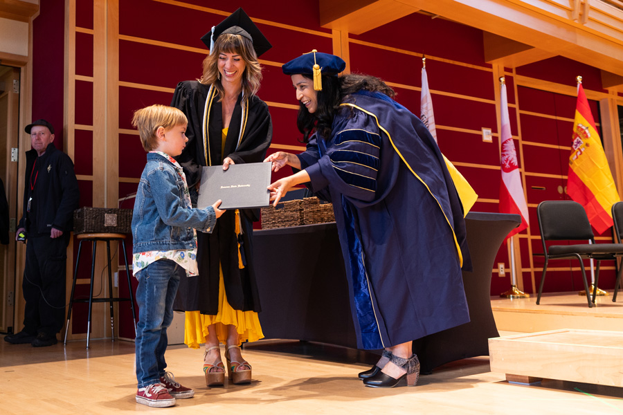 graduating students son accepts her diploma with her on stage